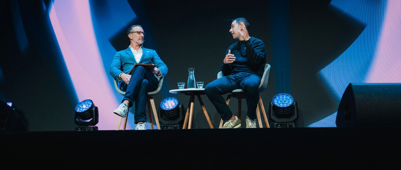 Dean McCoubrey, seated on the left in a teal blazer and glasses, moderating an on-stage conversation at World Summit AI 2026